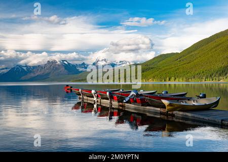 Barche a motore allineate su un molo che si riflette in un bellissimo lago con montagne innevate sullo sfondo del lago McDonald nel Glacier National Park Foto Stock