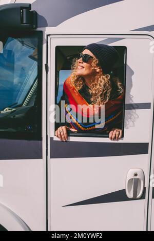 Buon turista fuori dalla finestra del camper godendo la destinazione. Una donna sorride e divertirsi ammirando il viaggio di arrivo sulla sua casa a motore. Van LIFE e. Foto Stock