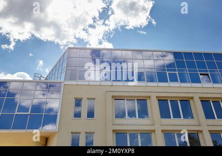 Le nuvole si riflettono nelle finestre del moderno edificio degli uffici. Esterno di un edificio moderno in una giornata di sole con un cielo blu Foto Stock