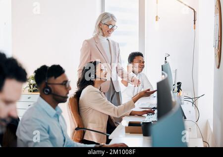 Non riesco a superare questo. una donna d'affari matura in piedi e che parla con due giovani agenti mentre usano i loro computer. Foto Stock