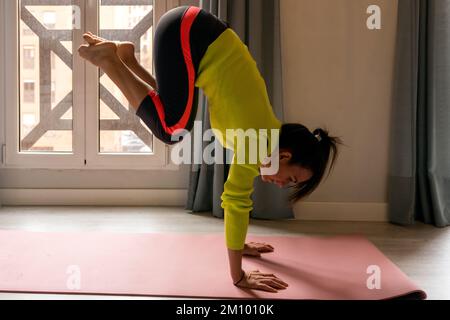 Giovane e forte donna, vestita di abbigliamento sportivo, esegue esercizi di calistenica sul pavimento dell'appartamento Foto Stock