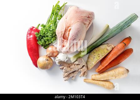 Ingredienti crudi per un brodo di pollo sano contro il freddo e l'influenza con verdure di radice, porro, zenzero, cipolla, aglio e peperone rosso su una schiena leggera Foto Stock
