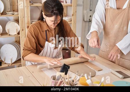 Amici con grembiuli in un laboratorio di ceramica preparare argilla per creare pezzi. Classe di artigianato. Foto Stock