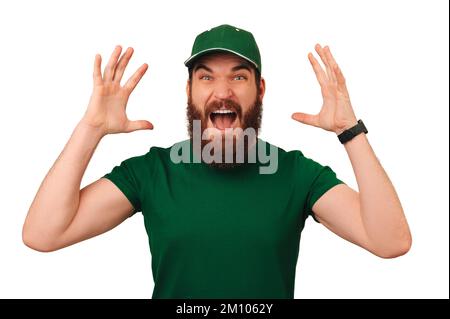 WOW dice che un uomo scosso bearded che indossa la divisa verde di consegna mentre urla a t la macchina fotografica con le mani in su. Foto Stock