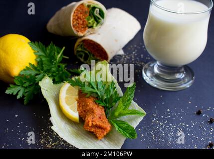 Presentazione di polpette crude su lattuga e limone su sfondo nero, primo piano turco 'cig kofte'. Foto Stock