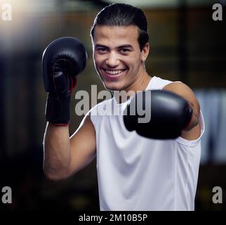 Ritratto, fitness e pugilato uomo punzonatura con i guanti di pugilato in una palestra sportiva per la salute. Atleta, pugile e volto di un forte personal trainer maschile Foto Stock