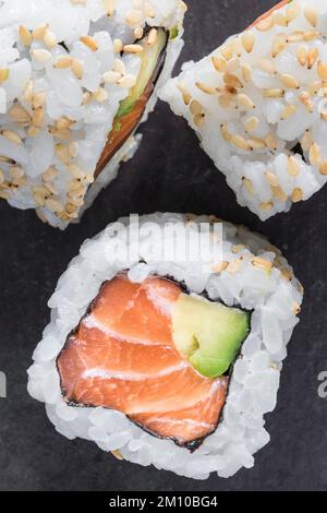 Uramaki di salmone e avocado con semi di sesamo su fondo nero. Vista dall'alto. Scatto macro Foto Stock