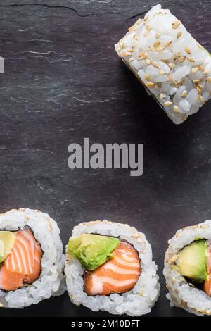 Uramakis di salmone e avocado con semi di sesamo su fondo nero. Vista dall'alto. Scatto macro. Spazio di copia. Foto Stock