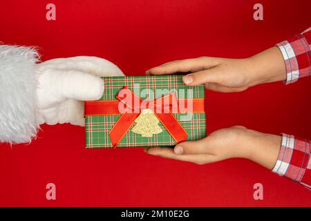 Le mani di Babbo Natale regalano ai bambini. sfondo rosso Foto Stock