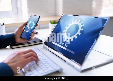 Man che esegue l'aggiornamento del software su telefono cellulare e laptop Foto Stock