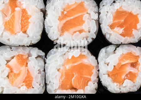 Macro vista dall'alto di 6 makis di salmone allineati su uno sfondo nero. Take away. Orientale, cucina giapponese. Spazio di copia. Foto Stock