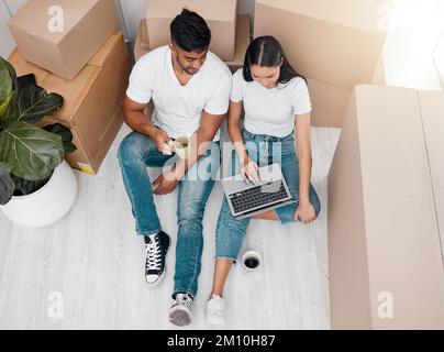 Ottenere idee di interior design. Ripresa ad angolo alto di una coppia irriconoscibile seduta nella nuova casa e con un notebook. Foto Stock