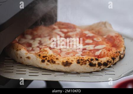 Pizza Margherita calda pronta a mangiare con salsa di pomodoro e mozzarella su tavola di legno, affumicata, primo piano Foto Stock