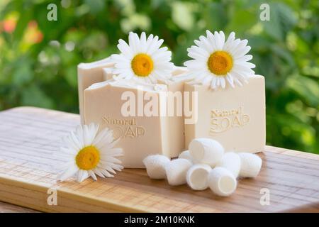 Sapone bianco fatto a mano con fiori di camomilla e bozzoli di seta su sfondo verde Foto Stock