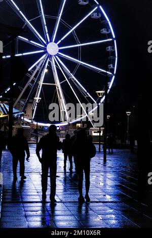 Un'immagine verticale delle silhouette delle persone, con la brillante ruota panoramica dietro di loro. Foto Stock