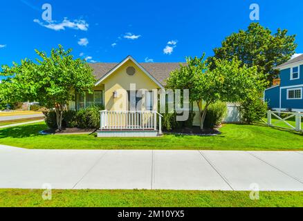 Piccola casa di famiglia gialla nelle giornate di sole con prato verde e sentiero in cemento Foto Stock