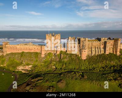 Il castello di Bamburgh, l'antica capitale del Regno di Northumbria, sorge sulla costa nord-orientale sotto un cielo azzurro. Il castello di Bamburgh è un forte imponente e un esempio di architettura normanna. Foto Stock