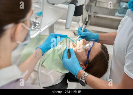 Medico esperto che conduce la rimozione del calcolo dentale al microscopio Foto Stock