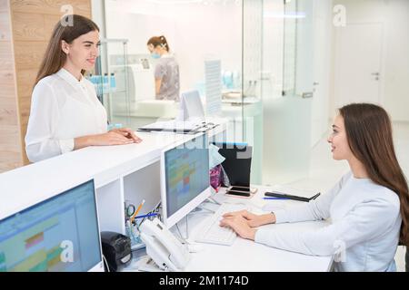Felice paziente donna che comunica con la segretaria amichevole in centro medico Foto Stock