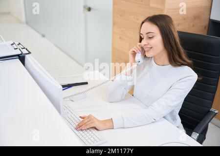 Una segretaria allegra parla al telefono alla reception Foto Stock