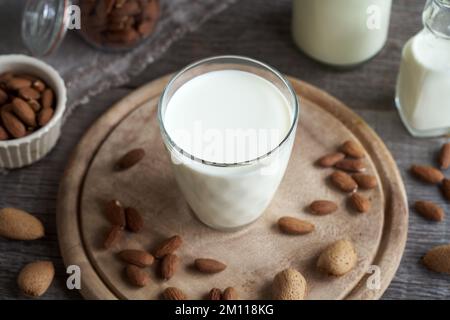 Un bicchiere di latte di mandorla vegana su un tavolo di legno, con mandorle intere e sgusciate sullo sfondo Foto Stock