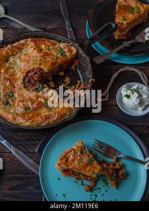 Torta di carne saporita con macinato di manzo piccante, ripieno di verdure in una padella di ghisa su un tavolo di legno Foto Stock