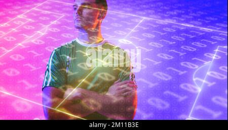 Sicuro giocatore caucasico con le braccia incrociate sul campo da calcio al neon e codifica binaria. Computer graphic, copy space, digital composite, calcio, design Foto Stock