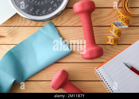 Piano di allenamento personale per il controllo del peso con attrezzature sportive e misurazione del corpo su un tavolo in legno e blocco note. Vista dall'alto. Foto Stock