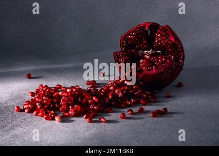 I semi di melograno rosso maturo vengono abbondantemente versati dal frutto. Frutta invernale di stagione. Fonte di ferro Foto Stock