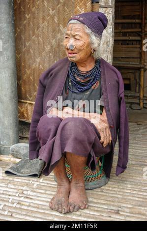 Ziro, Arunachal Pradesh, India - 02 24 2009 : Ritratto di una vecchia donna tribale di Apatani con tatuaggi facciali tradizionali e tappi per il naso seduti sullo sgabello Foto Stock