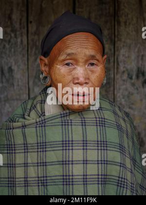 Mon, Nagaland, India - 03 03 2009 : Ritratto frontale della bella vecchia tribù Naga che indossa una plaid verde e una sciarpa nera su sfondo di legno scuro Foto Stock