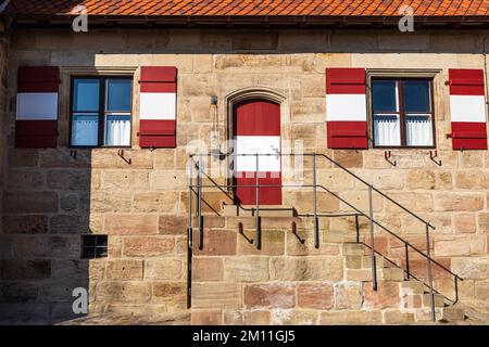 Facciata di un edificio in pietra con ingresso e finestre in rosso e bianco. Castello Imperiale. Norimberga, Baviera, Germania. Giorno di sole. Foto Stock