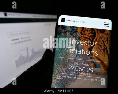 Persona che tiene il cellulare con la pagina web e il logo della società di tecnologia di viaggio Booking Holdings Inc. Sullo schermo. Messa a fuoco al centro del display del telefono. Foto Stock