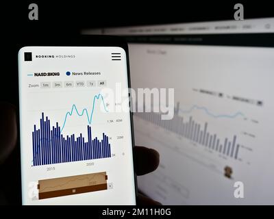 Persona che tiene in mano uno smartphone con una pagina Web e il logo della società di viaggi e tecnologia Booking Holdings Inc. Sullo schermo. Messa a fuoco al centro del display del telefono. Foto Stock