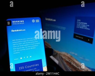 Persona in possesso di smartphone con sito web della società di tecnologia di viaggio Booking Holdings Inc. (rentalcars.com). Messa a fuoco al centro del display del telefono. Foto Stock