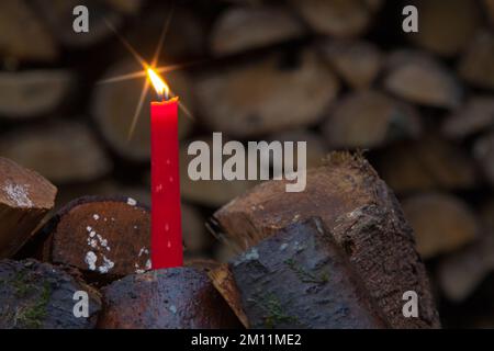 Lume di candela con una stella luminosa in una pila di legno, l'insolito motivo di Natale per la silvicoltura. Foto Stock