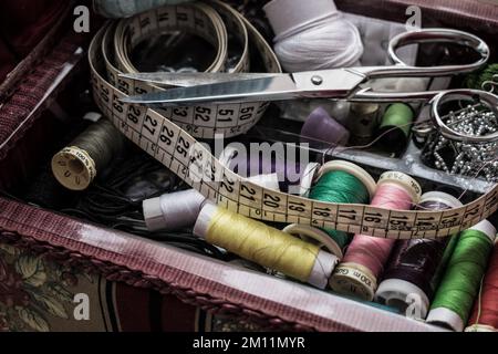 Fili colorati e vari accessori per la cucitura all'interno di una scatola da cucito Foto Stock