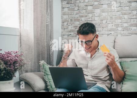 Un giovane uomo che usa il laptop e acquista sul negozio online. Ragazzo felice usando la carta di credito facendo acquisti da internet Foto Stock