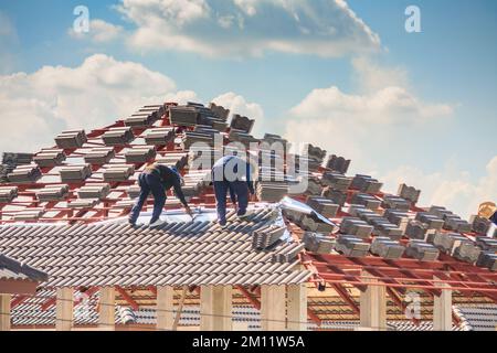 Costruzione di una casa. Tegole posa tegole sul tetto di un nuovo edificio Foto Stock
