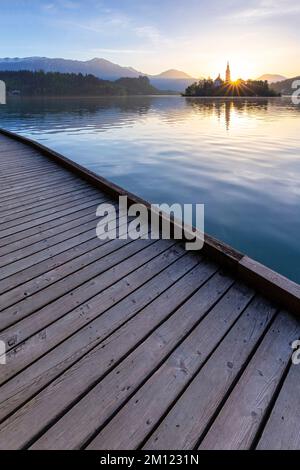 Vista della passerella in legno intorno al lago di Bled all'alba in primavera con la piccola isola e la chiesa dell'Assunzione di Maria. Bled, alta Carniola, Slovenia. Foto Stock