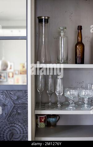 Vista in un armadio da cucina aperto con bicchieri e bottiglie decorati con cura Foto Stock