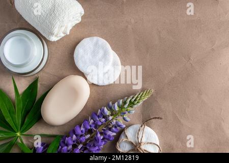 Cosmetici naturali biologici e fiori lupino su sfondo di carta artigianale. Crema idratante, sapone e asciugamano. Concetto di cura del corpo. Centro benessere e trattamenti di bellezza Foto Stock
