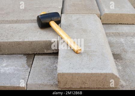 Martello per pavimentazione sfocato. Stack di pietre di pavimentazione. Pavimentazione in mattoni da giardino da parte di un'asfaltatrice professionista. Posa in opera di lastre di calcestruzzo grigie Foto Stock