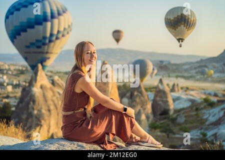 Donna turistica che guarda mongolfiere in Cappadocia, Turchia. Buon viaggio in Turchia concetto. Donna in cima a una montagna che gode di una vista meravigliosa Foto Stock