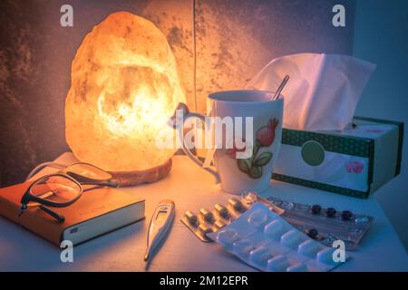 comodino illuminato da una lampada al sale, con farmaci e termometro per febbre Foto Stock