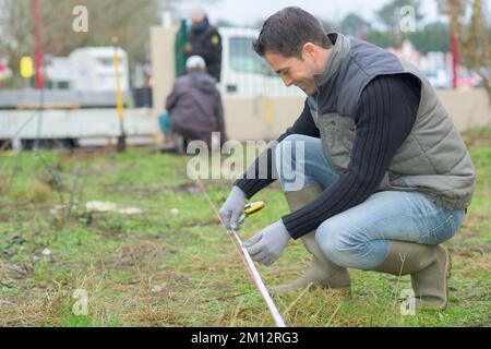 surveyor lavoratore che effettua la misurazione nel giardino Foto Stock