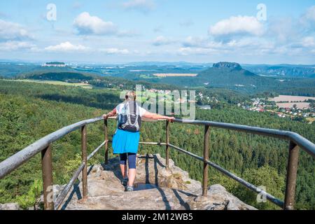 Donna anziana che fa escursioni sulle montagne di arenaria dell'Elba con vista sul Papststein in estate, la Svizzera sassone. Foto Stock