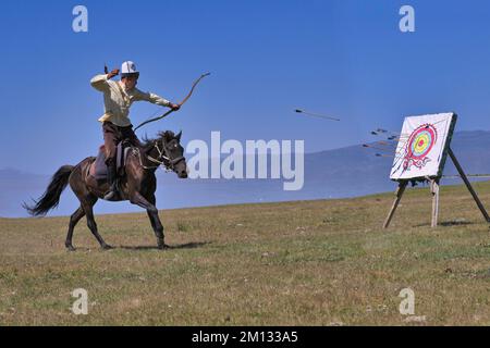 Il nomade del Kirghizistan spara frecce su un bersaglio mentre galoppa, il lago di Song kol, la regione di Naryn, il Kirghizistan, l'Asia Foto Stock