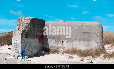 Un giovane che cammina di fronte a un bunker della seconda guerra mondiale sulla costa della città di Skagen, Danimarca Foto Stock