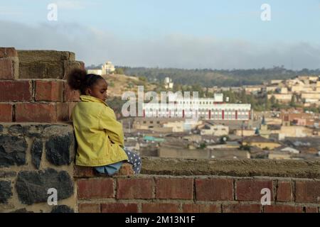 Giovane ragazza eritrea seduta su un muro che domina la città di Asmara Foto Stock